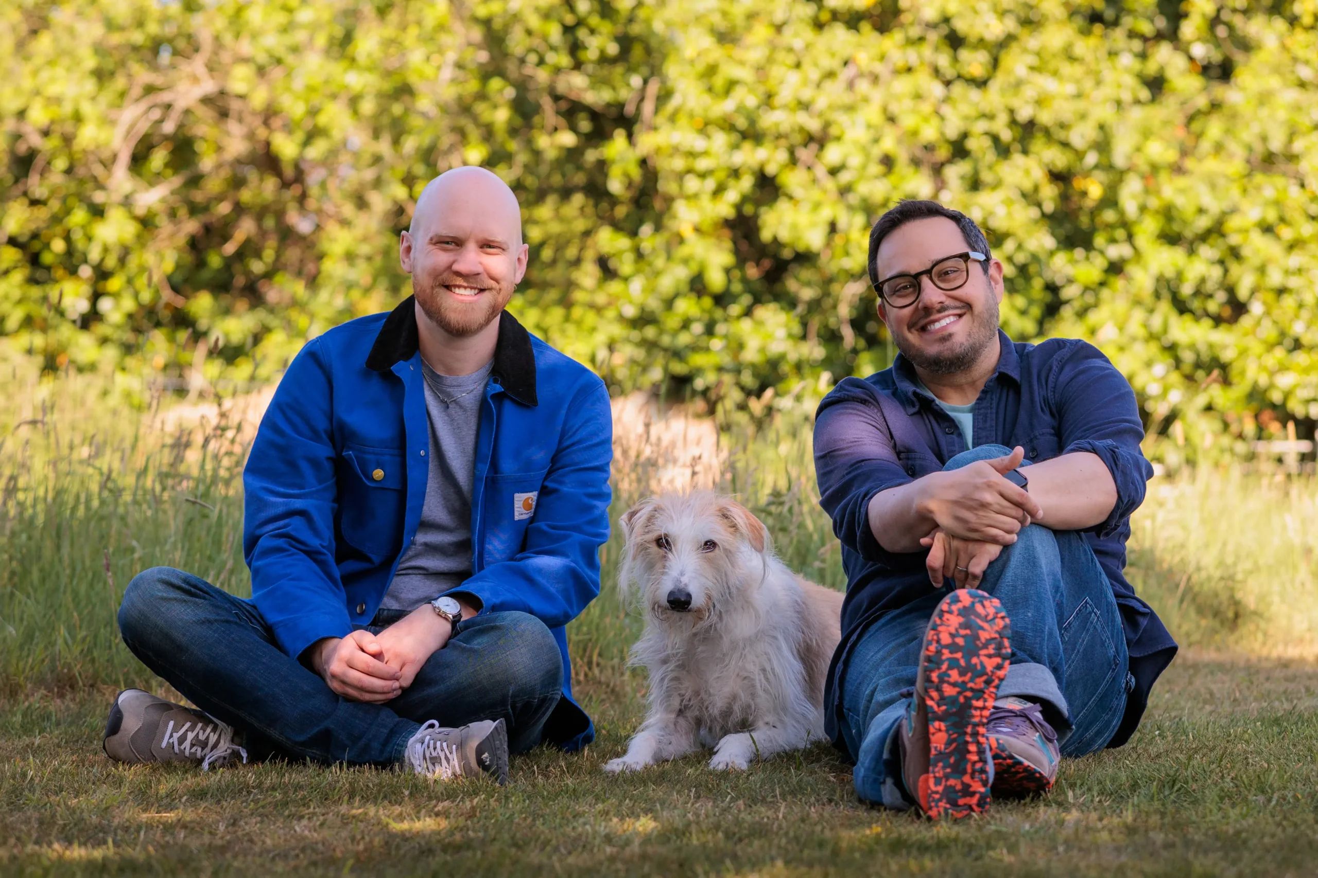 Steve and a friend sitting on the grass with a scruffy white dog